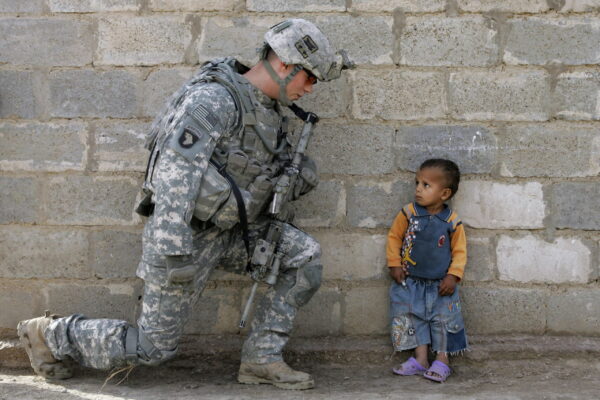 An American soldier on his knee looking at a frightened child from Iraq