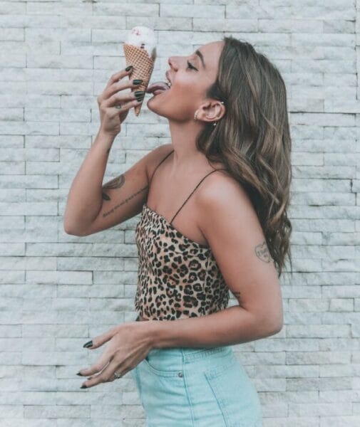 woman in an animal print top licking an ice cream cone