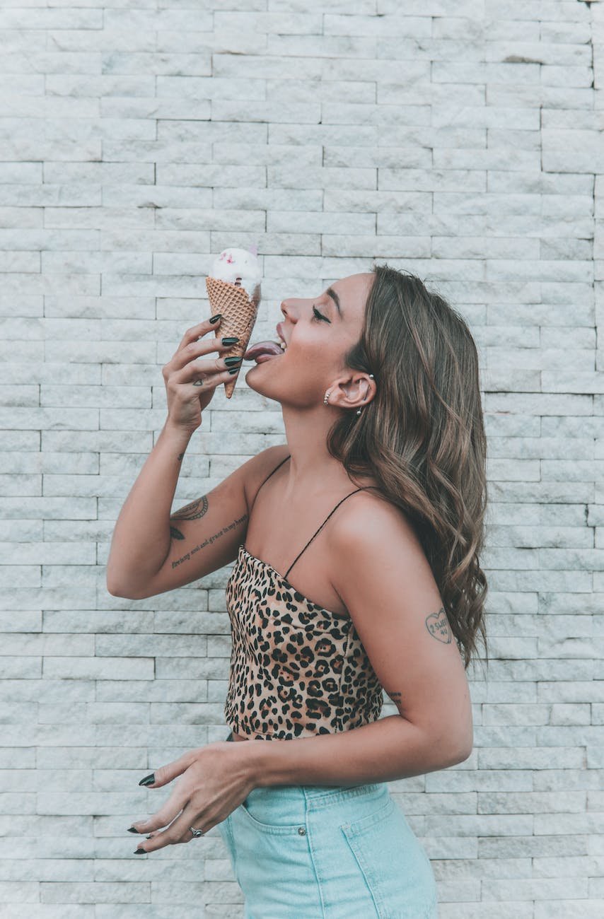 woman in an animal print top licking an ice cream cone