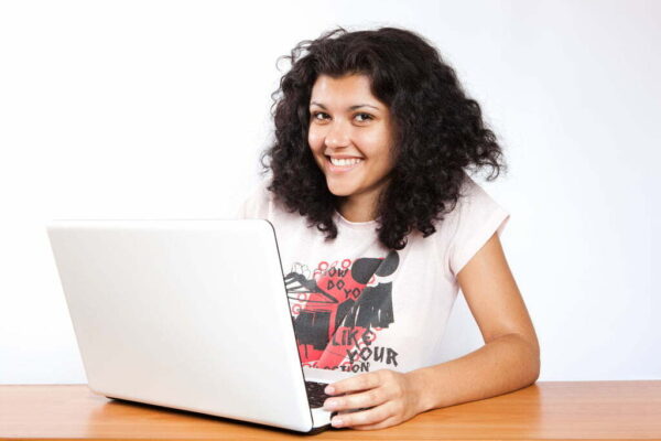 a young mixed race girl smiling at desk with a laptop in front of her
