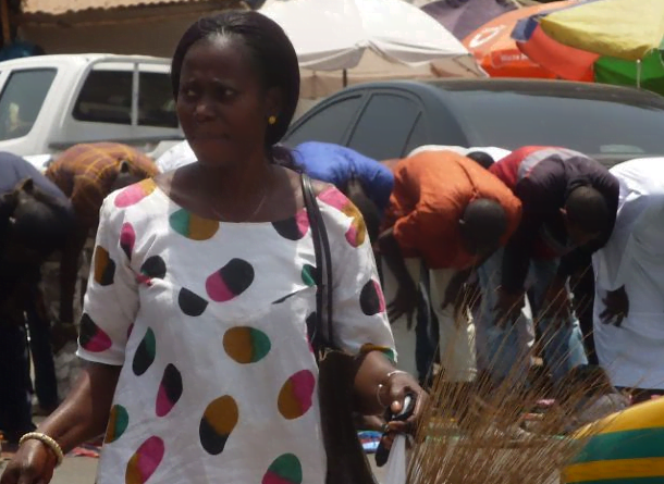 a lone woman shopping while men pray in The Gambia by Skendong Poetry