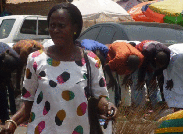 a lone woman shopping while men pray in The Gambia by Skendong Poetry
