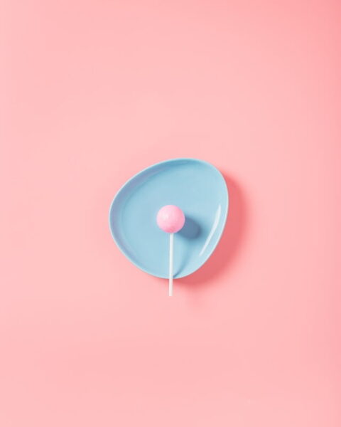 A pink lollipop on a blue bowl on a pink background.