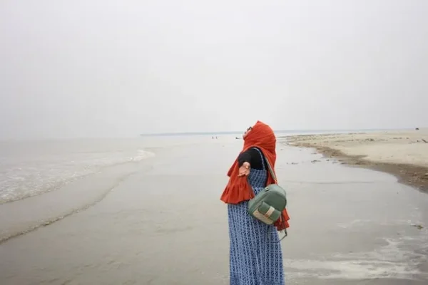 A woman in a red hijab standing by a cloudy beach. Photo by Refat Ul Islam / Unsplash