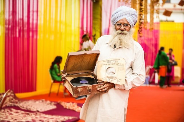 Man in white throbe holding vintage record player. Photo by Nischal Masand on Unsplash