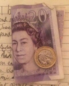 Image by Skendong Poetry containing writing on a piece of paper with a folded £20 pound note and a pound coin placed on top.