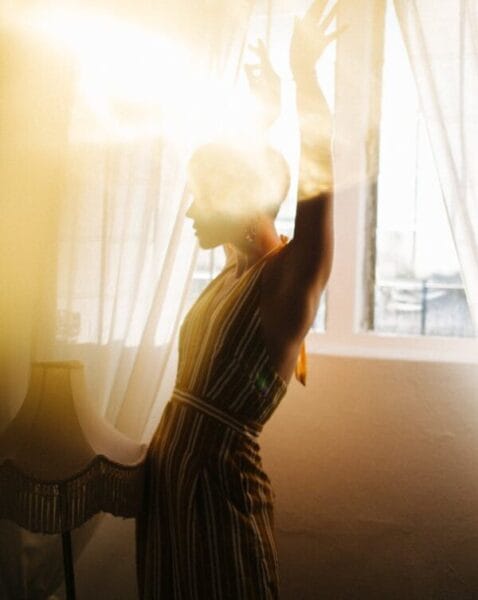 slender woman dancing near window in bright sunshine